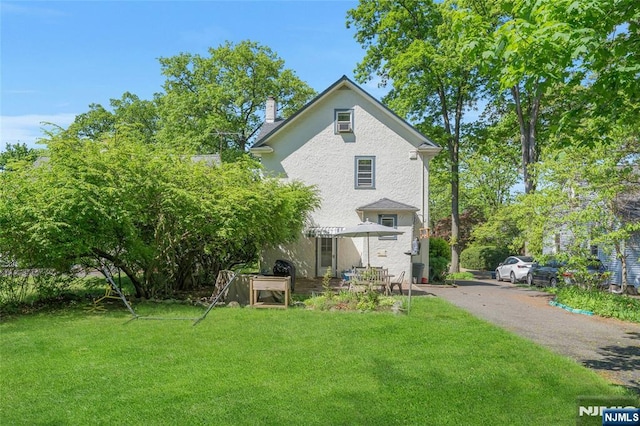 back of property featuring a yard, a chimney, and stucco siding