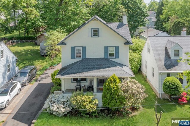 view of front of property featuring a porch, a chimney, stucco siding, a front yard, and a shingled roof