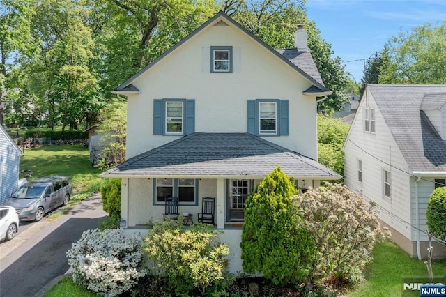 traditional home with a porch, a chimney, stucco siding, and roof with shingles