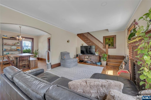 living area with wood finished floors, crown molding, stairway, arched walkways, and a chandelier