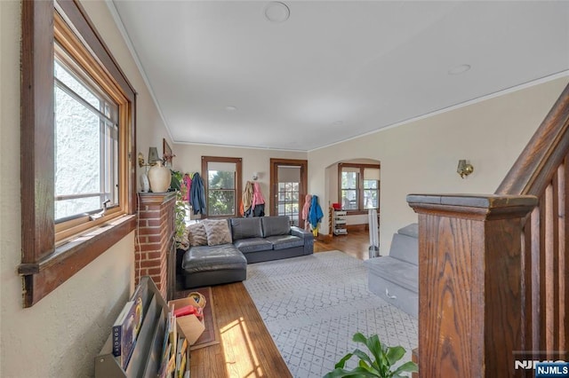living area with arched walkways, ornamental molding, and wood finished floors
