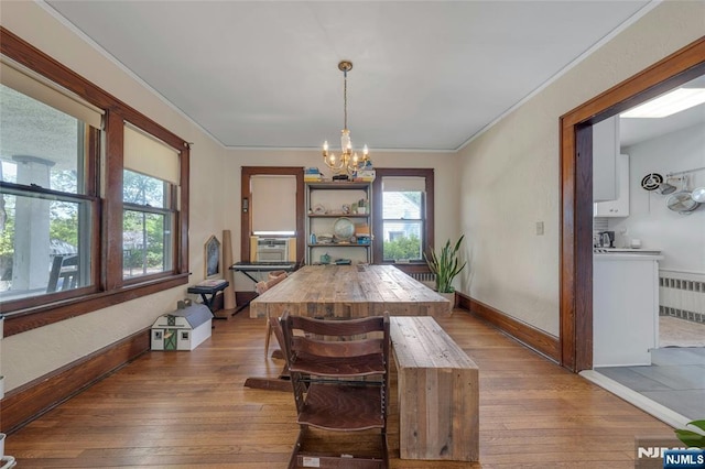 dining space with radiator, hardwood / wood-style flooring, a chandelier, ornamental molding, and baseboards