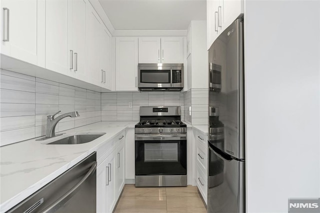 kitchen featuring stainless steel appliances, a sink, backsplash, white cabinets, and light stone counters