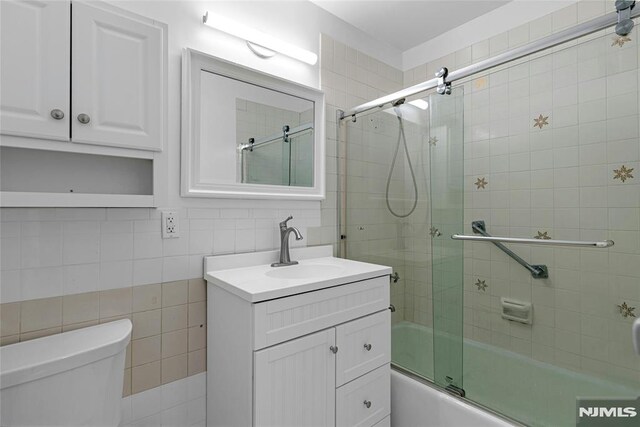 bathroom featuring tile walls, shower / bath combination with glass door, toilet, vanity, and tasteful backsplash