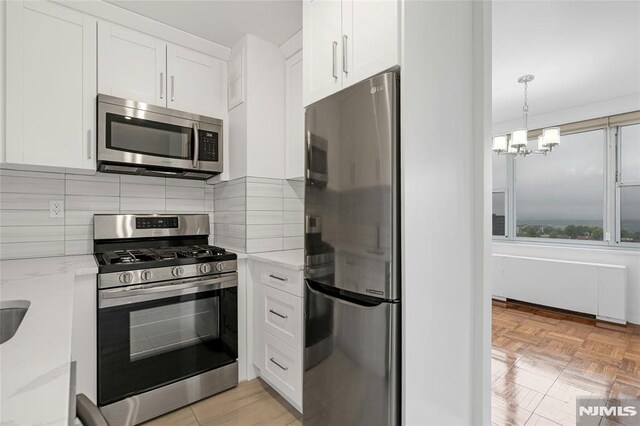 kitchen featuring stainless steel appliances, white cabinetry, backsplash, a chandelier, and light stone countertops