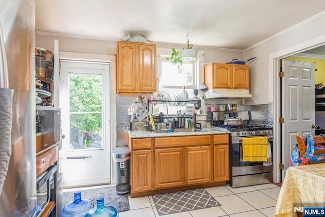 kitchen featuring stainless steel gas stove, light tile patterned floors, under cabinet range hood, a sink, and backsplash