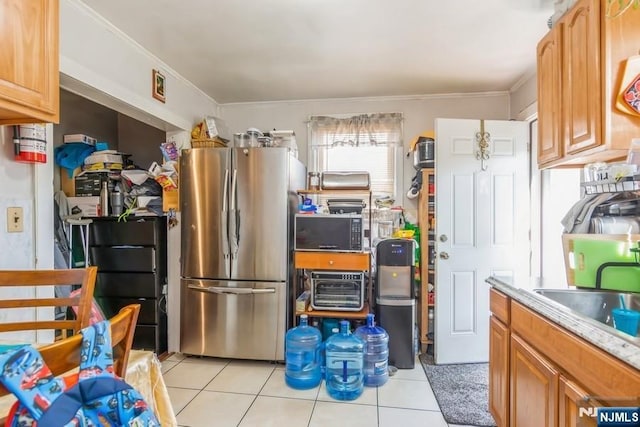 kitchen featuring black microwave, a sink, freestanding refrigerator, light tile patterned floors, and ornamental molding