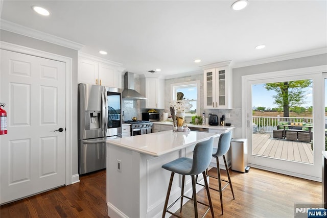 kitchen with white cabinetry, crown molding, wall chimney exhaust hood, backsplash, and stainless steel appliances