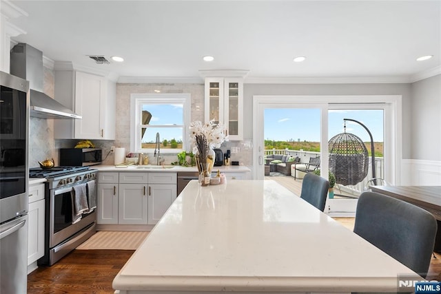 kitchen with visible vents, a sink, crown molding, wall chimney range hood, and stainless steel appliances