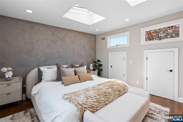 bedroom with a skylight, dark wood finished floors, visible vents, an accent wall, and recessed lighting