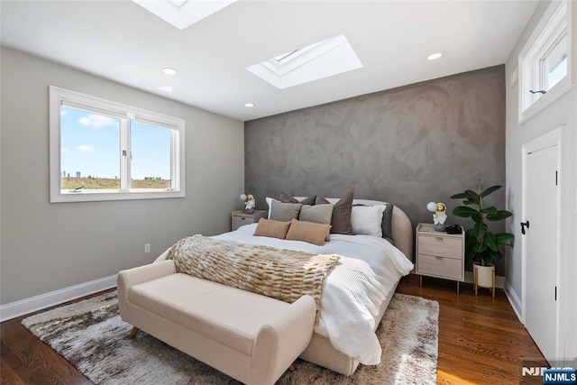 bedroom featuring an accent wall, a skylight, baseboards, and wood finished floors