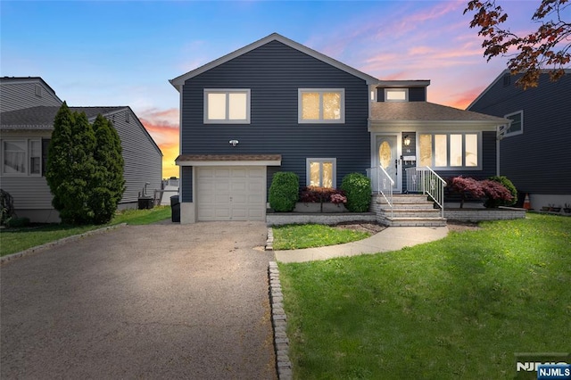 tri-level home featuring aphalt driveway, roof with shingles, a garage, and a lawn