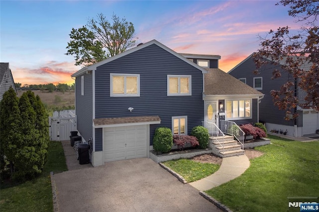 split level home with roof with shingles, driveway, a garage, and a front yard