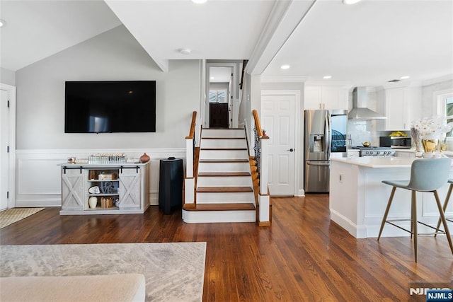 interior space featuring stainless steel appliances, a breakfast bar area, wall chimney exhaust hood, dark wood-style flooring, and white cabinets