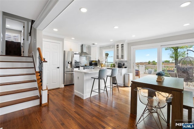 kitchen featuring glass insert cabinets, wall chimney exhaust hood, crown molding, white cabinetry, and a kitchen island