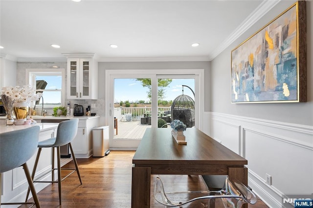 dining room with a wainscoted wall, plenty of natural light, ornamental molding, and light wood-style floors