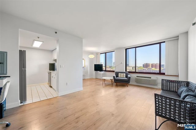 living room with an AC wall unit, baseboards, and light wood-type flooring