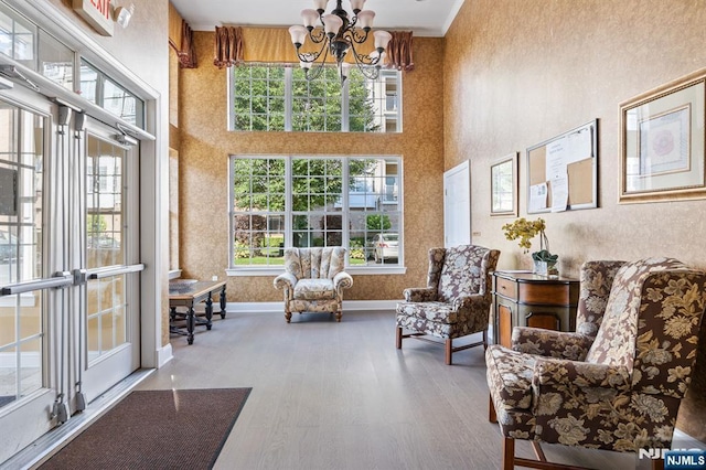 sitting room featuring baseboards, a notable chandelier, a towering ceiling, and wood finished floors