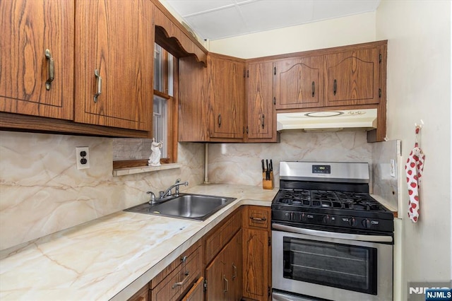 kitchen with under cabinet range hood, gas stove, a sink, and brown cabinetry