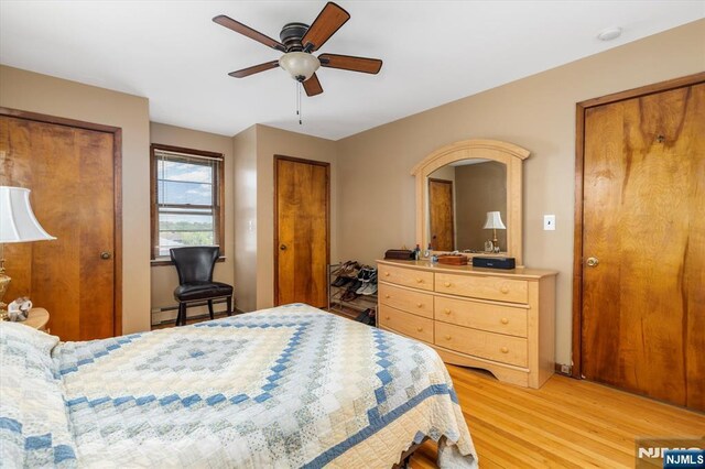 bedroom with multiple closets, light wood-style floors, a baseboard heating unit, and a ceiling fan