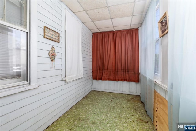 unfurnished room featuring tile patterned floors, a drop ceiling, and wood walls