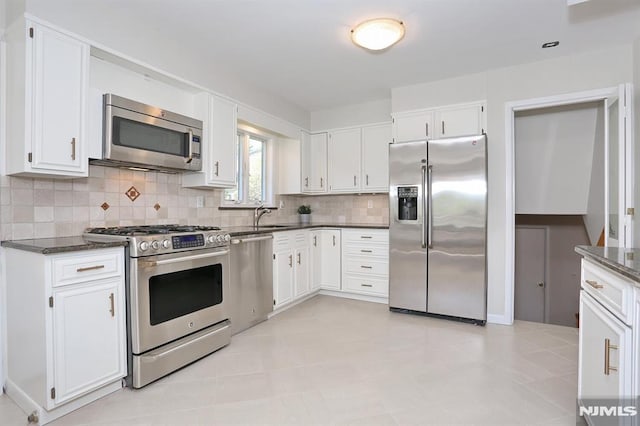 kitchen with a sink, white cabinetry, decorative backsplash, stainless steel appliances, and dark stone counters