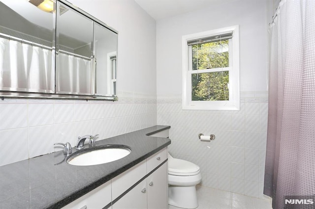bathroom with toilet, a wainscoted wall, tile patterned floors, tile walls, and vanity