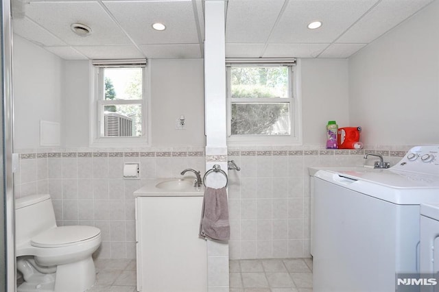 bathroom featuring tile walls, toilet, vanity, tile patterned floors, and a paneled ceiling