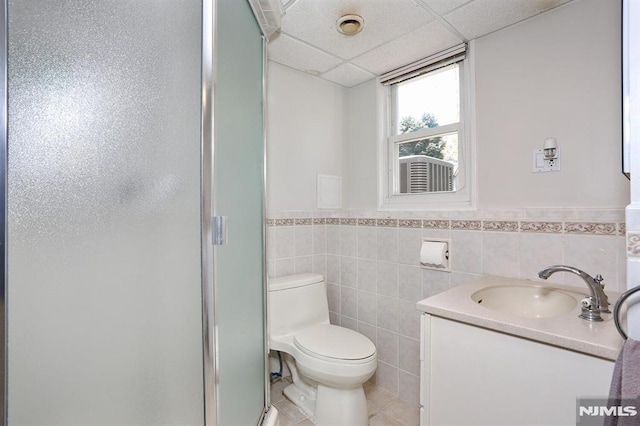 bathroom with a stall shower, a drop ceiling, toilet, wainscoting, and vanity