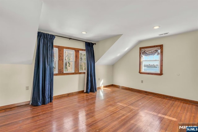 additional living space featuring vaulted ceiling, plenty of natural light, visible vents, and wood-type flooring