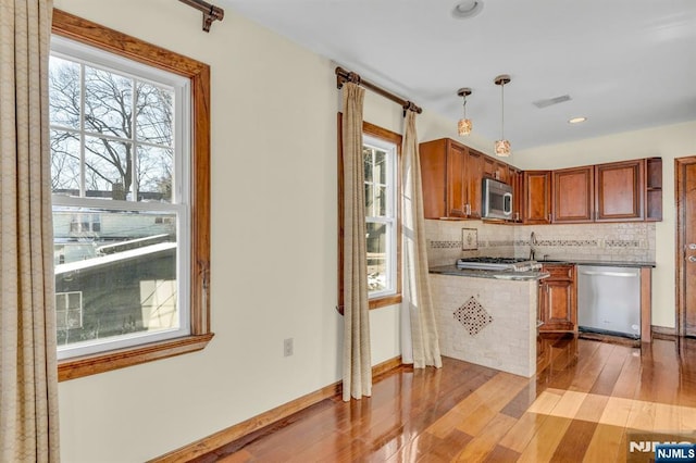 kitchen with light wood-style flooring, visible vents, brown cabinets, stainless steel appliances, and tasteful backsplash