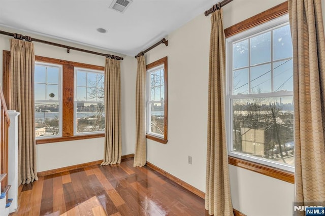 empty room with a wealth of natural light, visible vents, wood finished floors, and baseboards