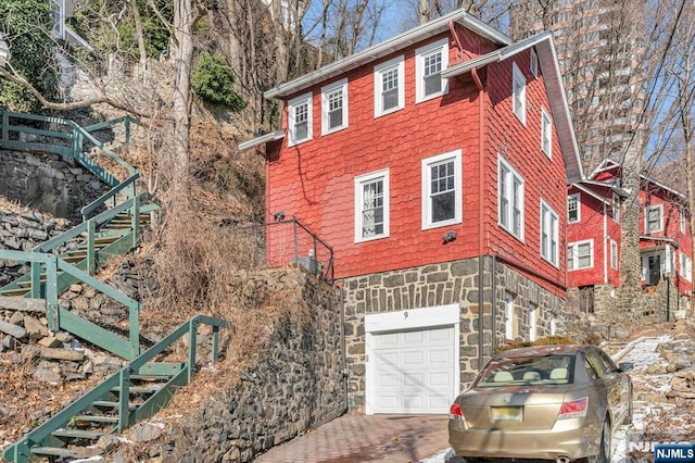 view of home's exterior featuring an attached garage, stairway, driveway, and stone siding