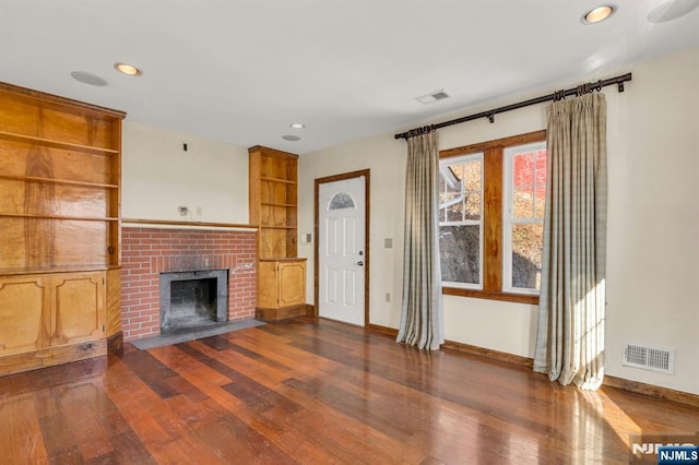 unfurnished living room featuring a brick fireplace, baseboards, dark wood-type flooring, and visible vents
