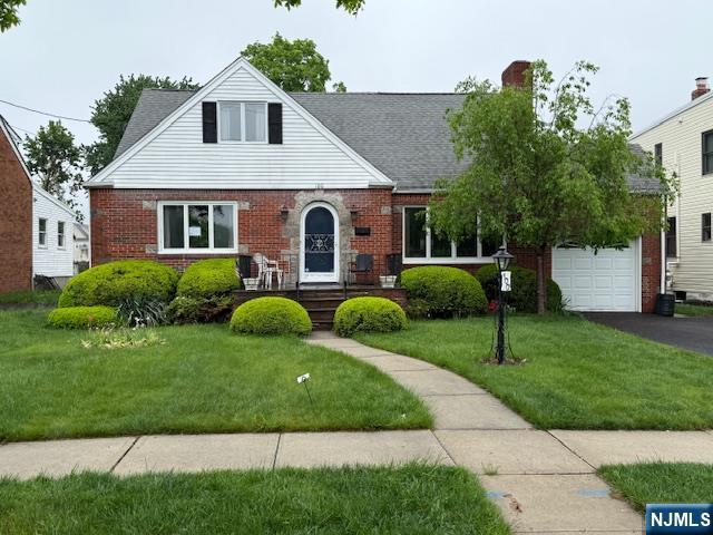 view of front of property featuring a front lawn, brick siding, driveway, and a chimney