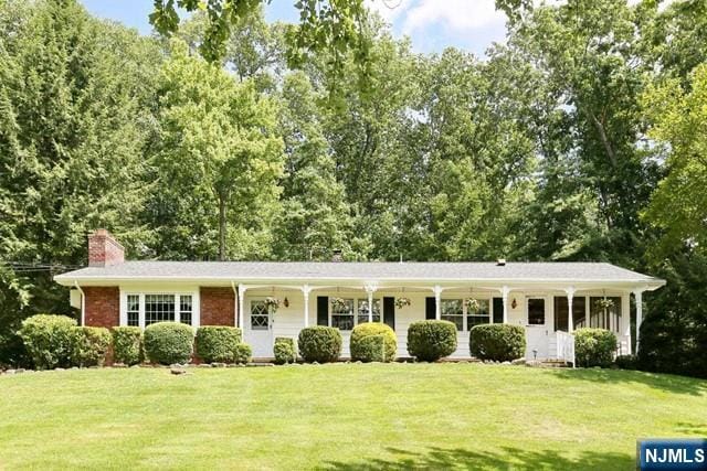 view of front of home with covered porch, a chimney, and a front yard