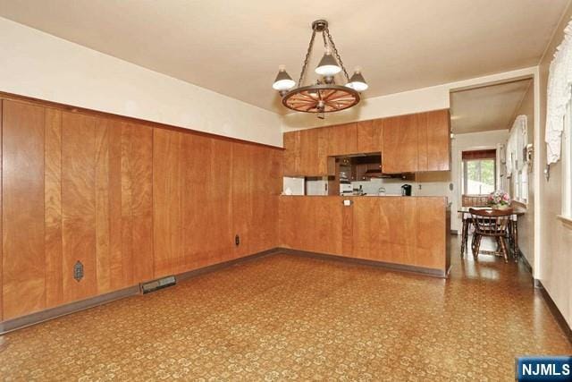 kitchen with a peninsula, an inviting chandelier, brown cabinets, dark floors, and decorative light fixtures