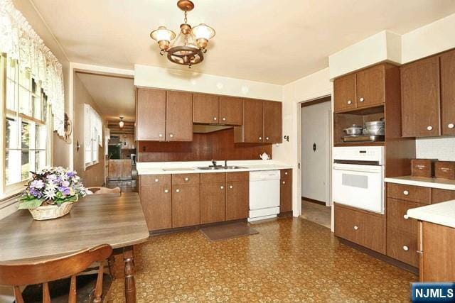 kitchen featuring a chandelier, brown cabinets, a sink, and white appliances