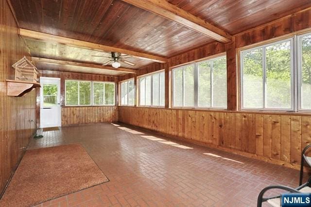 unfurnished sunroom with wood walls, brick floor, wood ceiling, and a ceiling fan