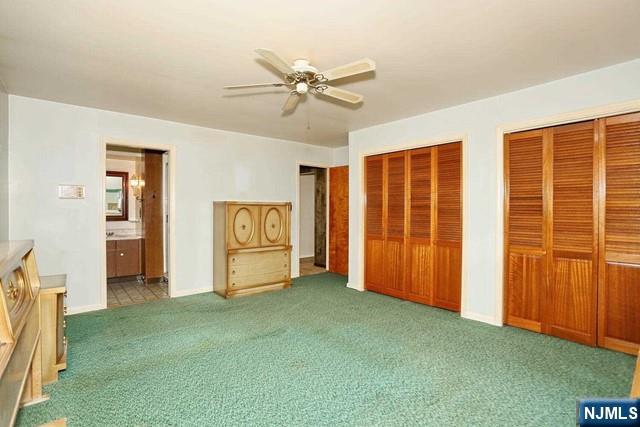 unfurnished bedroom featuring ensuite bathroom, two closets, carpet floors, a ceiling fan, and baseboards