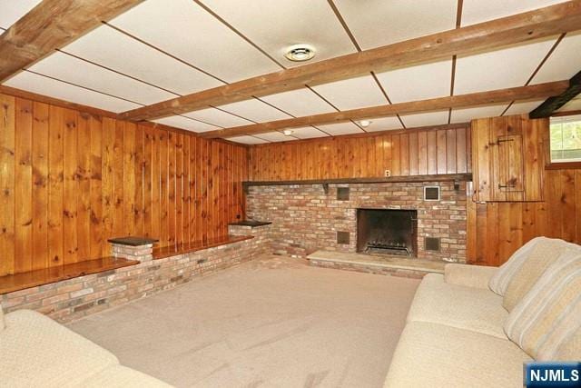 carpeted living area featuring brick wall, wood walls, a brick fireplace, and beamed ceiling
