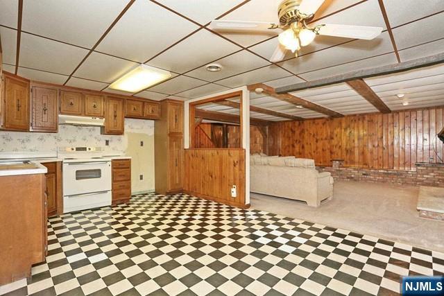 kitchen with under cabinet range hood, white electric range, wooden walls, open floor plan, and light countertops