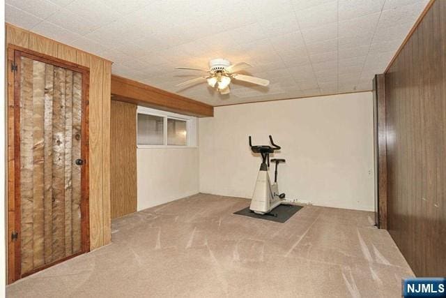 exercise room featuring wooden walls, carpet, and a ceiling fan
