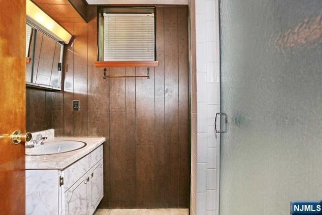 bathroom featuring a shower stall, wood walls, and vanity