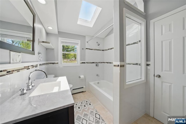 full bath with tile walls, shower / bath combination, a baseboard heating unit, vanity, and a skylight