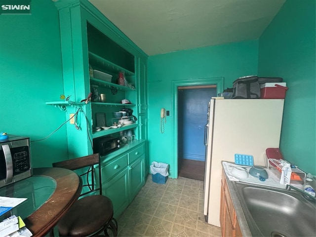 kitchen with a sink, stainless steel microwave, and freestanding refrigerator