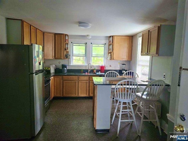 kitchen with freestanding refrigerator, open shelves, dark countertops, and brown cabinetry