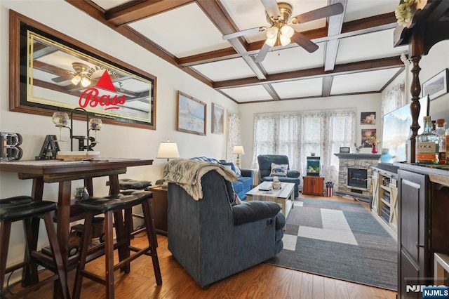 living area featuring ceiling fan, coffered ceiling, a fireplace, wood finished floors, and beam ceiling