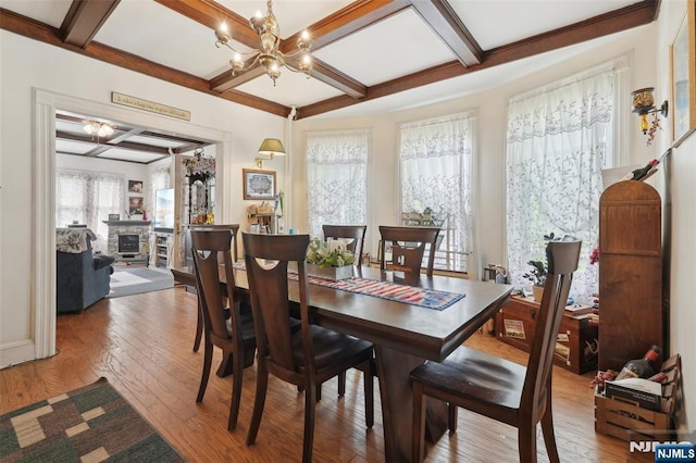 dining area with coffered ceiling, light wood-style flooring, a chandelier, beamed ceiling, and a stone fireplace