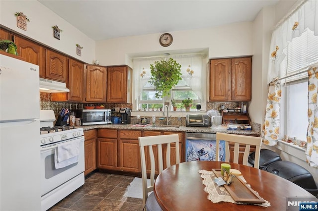 kitchen featuring appliances with stainless steel finishes, under cabinet range hood, a sink, brown cabinetry, and decorative backsplash